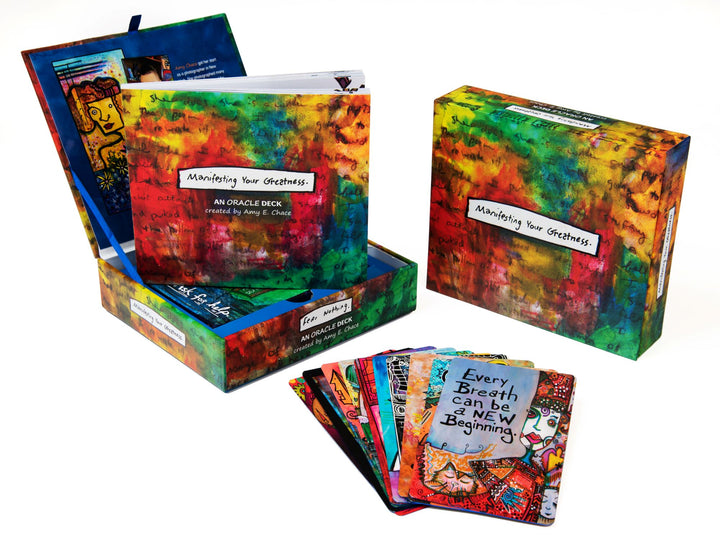 Manifesting Your Greatness by Schiffer Publishing, Ltd. is a colorful oracle deck with illustrated wisdom cards, a vibrant storage box, and a guidebook—featuring artistic designs and motivational phrases for inspiration.