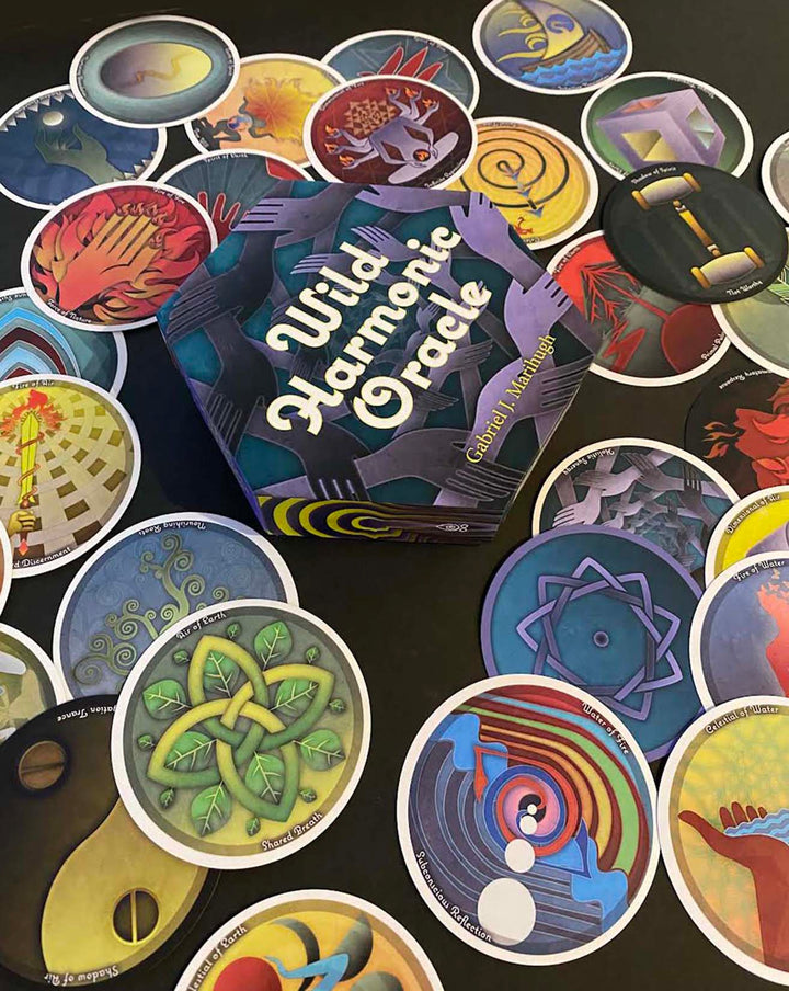 A hexagonal box labeled Wild Harmonic Oracle Cards from Schiffer Publishing, Ltd. is surrounded by vibrant chakra cards with abstract designs, each inspired by energy alchemy and spread out in a colorful fan shape.