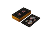 A stack of Nocturnal Garden Lenormand cards by Schiffer Publishing, Ltd. is shown with gold edges. One card displays a teapot, cup, and heart-shaped steam in whimsical art; the card backs have celestial and floral designs on black.