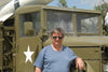 A man in sunglasses and a blue t-shirt stands outside on a sunny day beside an olive green Sd.Kfz. 251 half-track (Schiffer Publishing, Ltd.) with a white star. A portion of a missile is visible atop the vehicle.