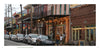 A row of parked cars lines a lively French Quarter street with colorful buildings, string lights, and outdoor seating—capturing the vibrant spirit found in "New Orleans" by Schiffer Publishing, Ltd.