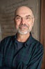 A middle-aged man with glasses, a bald head, and a gray beard smiles in a green and blue plaid shirt before a textured background—reflecting his passion featured in Weave with Words by Schiffer Publishing, Ltd.