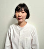 A person with short black hair wears the "Wild Embroidery" white shirt by Schiffer Publishing, Ltd., featuring nature-inspired embroidery, standing against a plain light background and gazing to the side with a neutral expression.