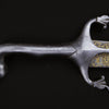 Close-up of a steel sword hilt with a curved handle and ornate crossguard from Weapons of Warriors by Schiffer Publishing, Ltd. The blade, inspired by historical swords, showcases gold patterns and calligraphy near the base against a black background.