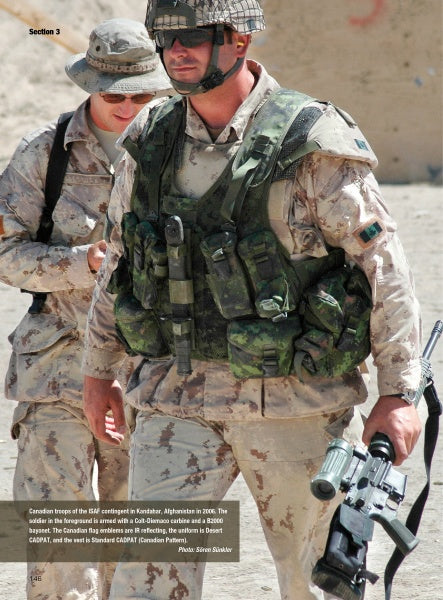 Two soldiers in desert camo stand outdoors. A U.S. Marine with sunglasses and helmet holds a rifle; military knives, featured in "Modern Knives in Combat" by Schiffer Publishing, Ltd., are attached to his tactical vest. Sandy background.