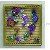 Flower Jewelry by Schiffer Publishing, Ltd. features vibrant wire and foil flowers, resembling brooches crafted from repurposed chocolate wrappers, beautifully arranged on a ridged beige background within a square box.