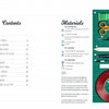 A table of contents from Schiffer Publishing, Ltd.’s "Little Paper Universes" appears on the left, while the right shows scissors, glue, tape, pencils, a ruler, and craft supplies on a green cutting mat.